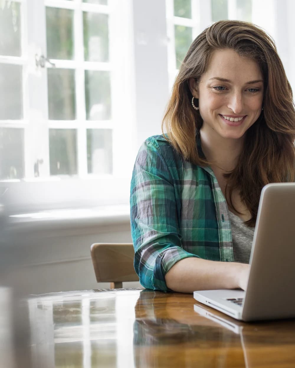 A smiling woman working on a laptop at a wooden table