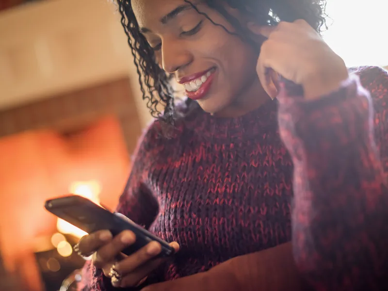 A woman smiling at a message on her phone beside a fire
